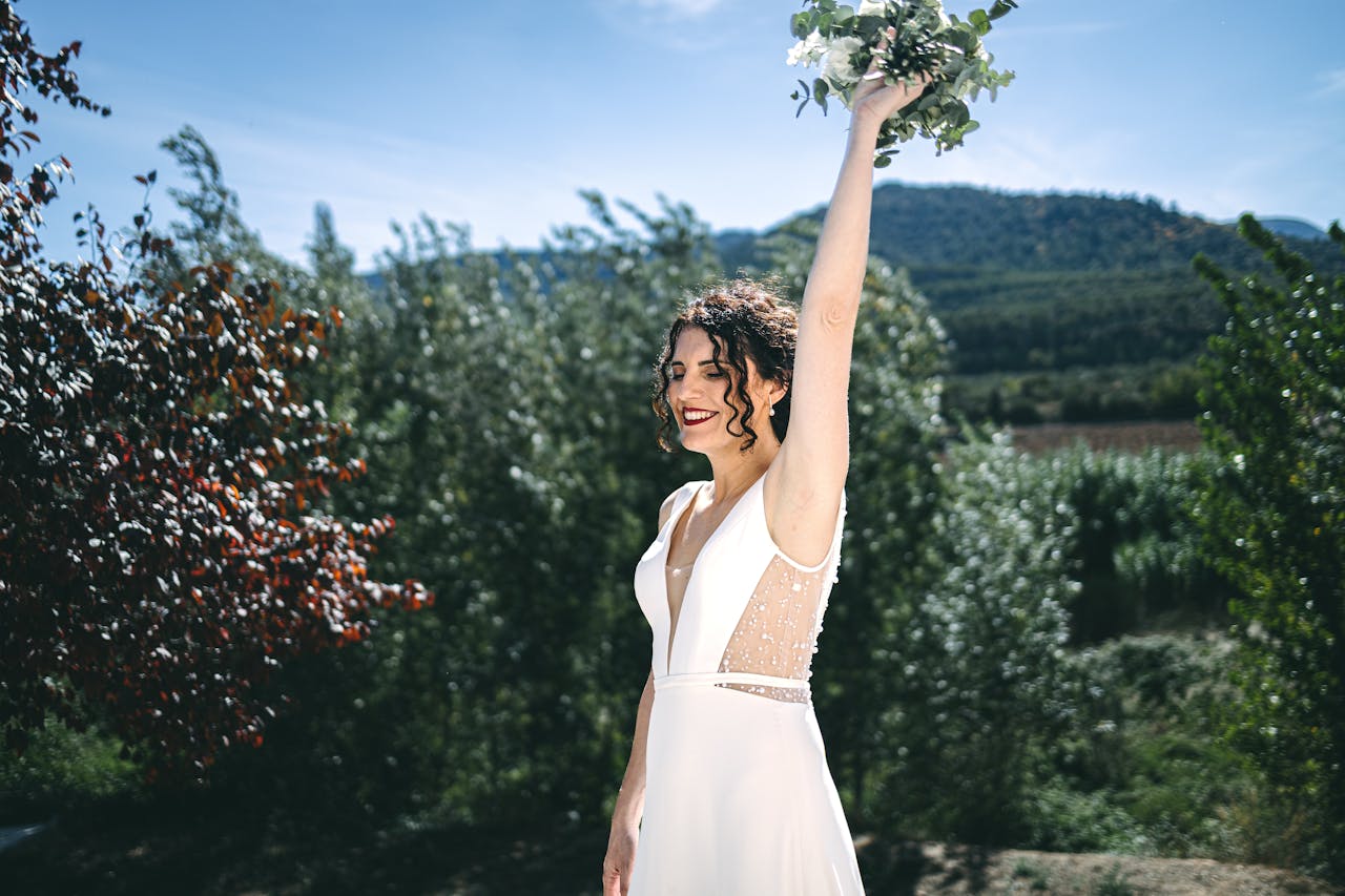 hero-img-01 A smiling bride raises her bouquet in a vibrant outdoor setting, embracing nature and joy.