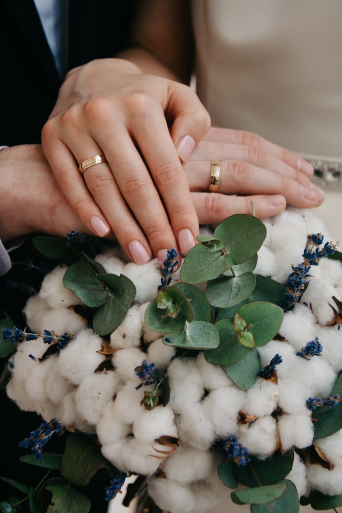our-services-1 Close-up of couple's hands with gold wedding bands over a floral bouquet.